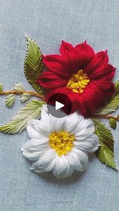 two white and red flowers with green leaves on a blue cloth background that is stitched together