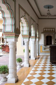 an ornately decorated hallway with columns and potted plants on the floor in front of it