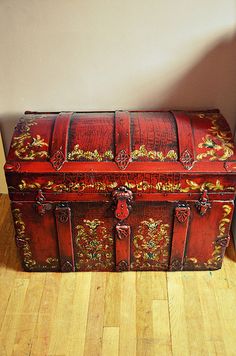 an old red trunk sitting on top of a hard wood floor next to a wall