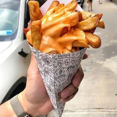 a hand holding a paper cone filled with french fries on the side of a street