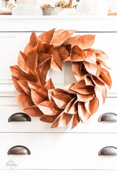 a wreath is hanging on the wall above a white dresser with drawers and knobs