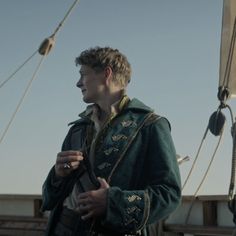 a man standing on top of a boat wearing a green jacket and holding a cell phone