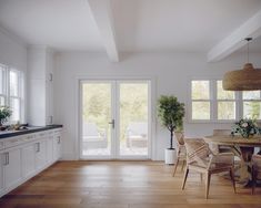 a kitchen with white walls and wooden floors has an open door leading to the outside