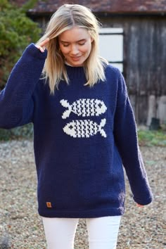 a woman wearing a blue sweater with white fish drawn on the front and back, standing in gravel