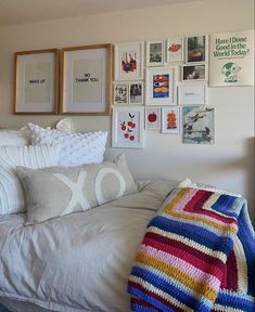 a bed covered in lots of pictures and blankets next to a wall with framed pictures on it