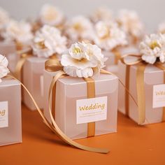 wedding favors wrapped in pink paper with gold ribbon and white flowers on each side, sitting on an orange surface