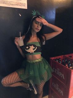 a woman in a green outfit leaning against a wall holding a drink and posing for the camera