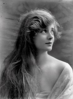 an old black and white photo of a woman with long hair in a dress looking off to the side