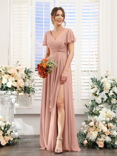 a woman standing in front of flowers wearing a long pink bridesmaid dress with thigh high slit