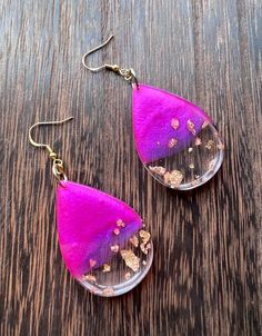 two pink tear shaped earrings with gold flakes on them sitting on top of a wooden table