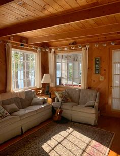 a living room with two couches and a guitar on the floor in front of windows