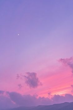 an airplane is flying in the sky at sunset with mountains in the background and pink clouds