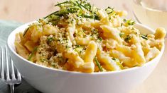 a white bowl filled with macaroni and cheese next to a glass of wine