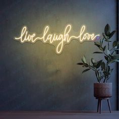 a neon sign that says live laugh love on the wall next to a potted plant