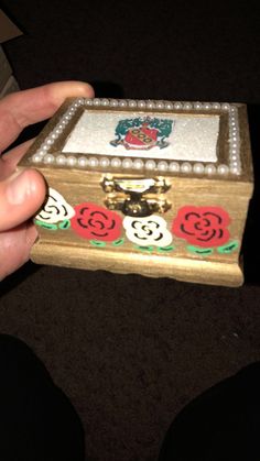 a hand holding a small wooden box with roses on it