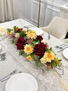 the table is set with white plates, silverware and colorful flowers in vases