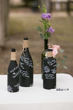 three black bottles with writing on them are sitting on a table next to a flower vase