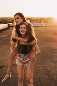 two young women are hugging each other in the middle of an empty parking lot at sunset