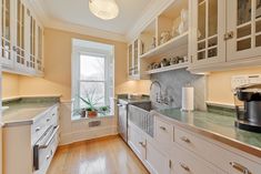 a large kitchen with white cabinets and wood flooring on the walls, along with an open window