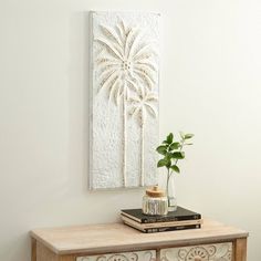 a table with a vase and some books on top of it next to a wall hanging