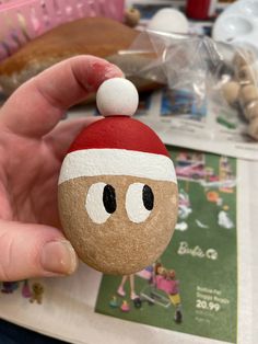 a hand holding a rock with a face painted on it and a santa hat on top