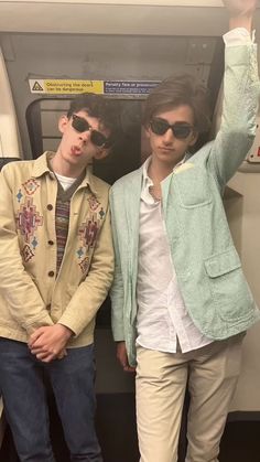 two young men standing next to each other in front of a train door with their arms up