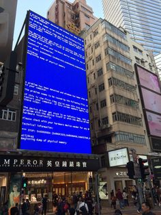 a large blue screen on the side of a building in a busy city street with people walking around