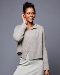 a woman is smiling and posing for the camera with her hand on her head while wearing a gray skirt