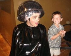 two boys dressed up as batman and robin wayne in the living room, one is wearing a plastic hat