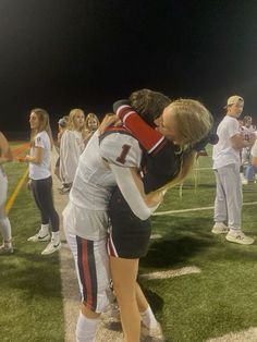 two female football players hugging each other on the sidelines at night with fans in the background