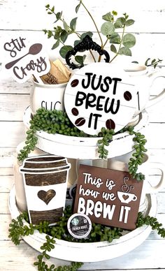 some coffee mugs and signs are stacked on top of each other with greenery