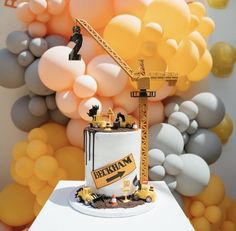 a construction themed birthday cake on a table in front of balloons and a crane behind it