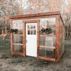 a small wooden shed with two doors and plants in the top window, on grass