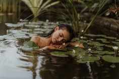 a woman is floating in the water with lily pads on her chest and head resting on her hand