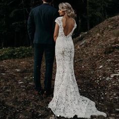 a bride and groom standing in the woods looking at each other with their back to the camera