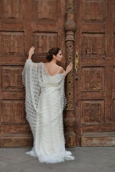 a woman in a wedding dress leaning against a wooden door with her arms on the wall