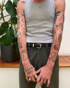 a man with many tattoos on his arm and chest standing in front of a potted plant