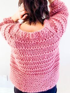 a woman is wearing a pink sweater and has her hands on her head as she stands in front of a white wall