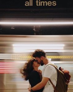 a man and woman are kissing in front of a subway sign that says all times