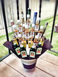 an arrangement of liquor bottles in a bucket on a table outside with grass and fence behind it