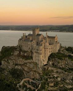 an old castle sitting on top of a cliff next to the ocean in front of a sunset