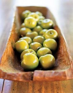 a wooden bowl filled with green apples on top of a table