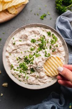 a hand holding a cracker over a bowl of dip