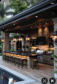 an outdoor kitchen and dining area next to a swimming pool with lights on the ceiling