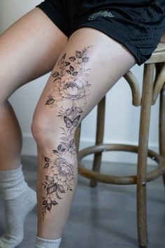 a woman sitting on a stool with her legs crossed and flowers tattooed on the leg