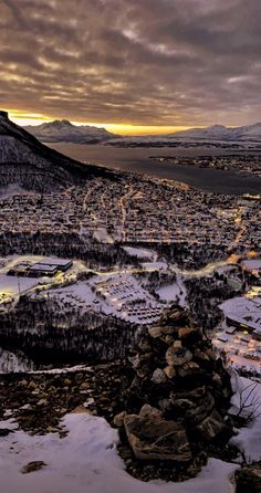 a snow covered mountain with a city in the distance and mountains behind it at sunset