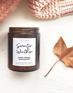 a candle next to some leaves on a white surface with a pink blanket and sweater