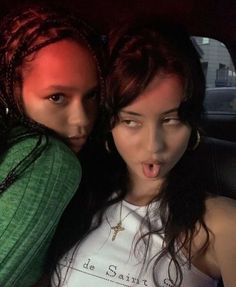 two young women sitting in the back seat of a car, making faces with their mouths open