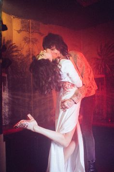 a man and woman are kissing in front of a red light on the dance floor