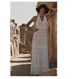 a woman in a white crochet dress standing next to a stone wall with her hands on her hips